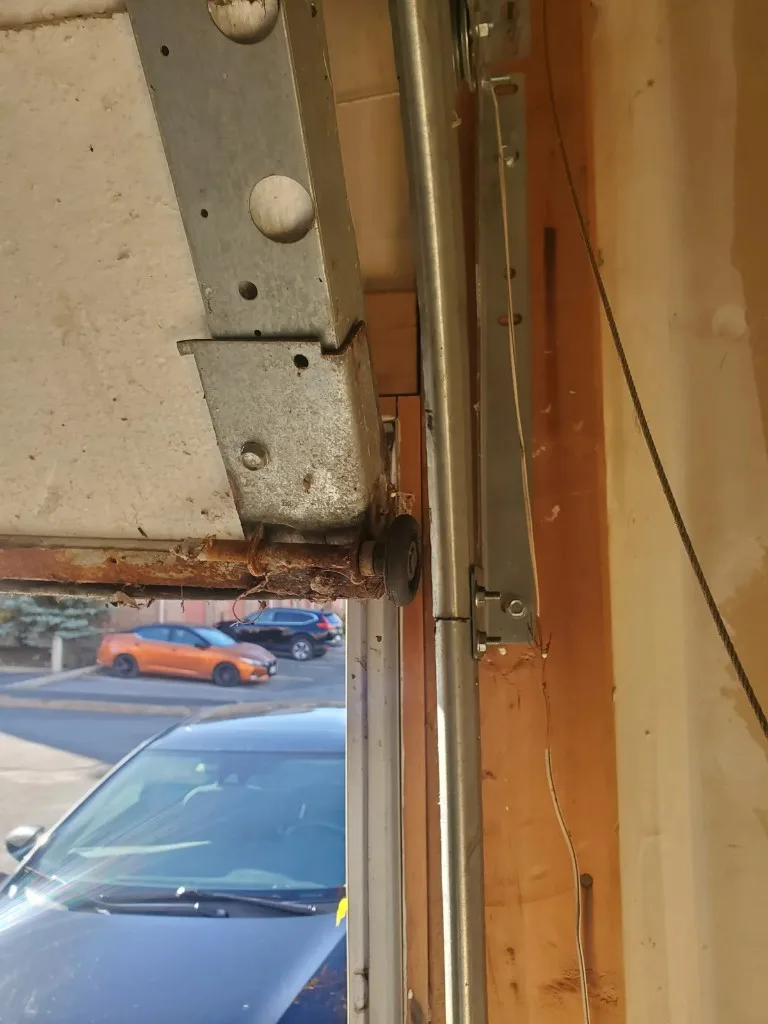 Rusted bottom bracket and corroded bottom retainer on a Barrhaven garage door, with the roller in the track and the lift cable at the side