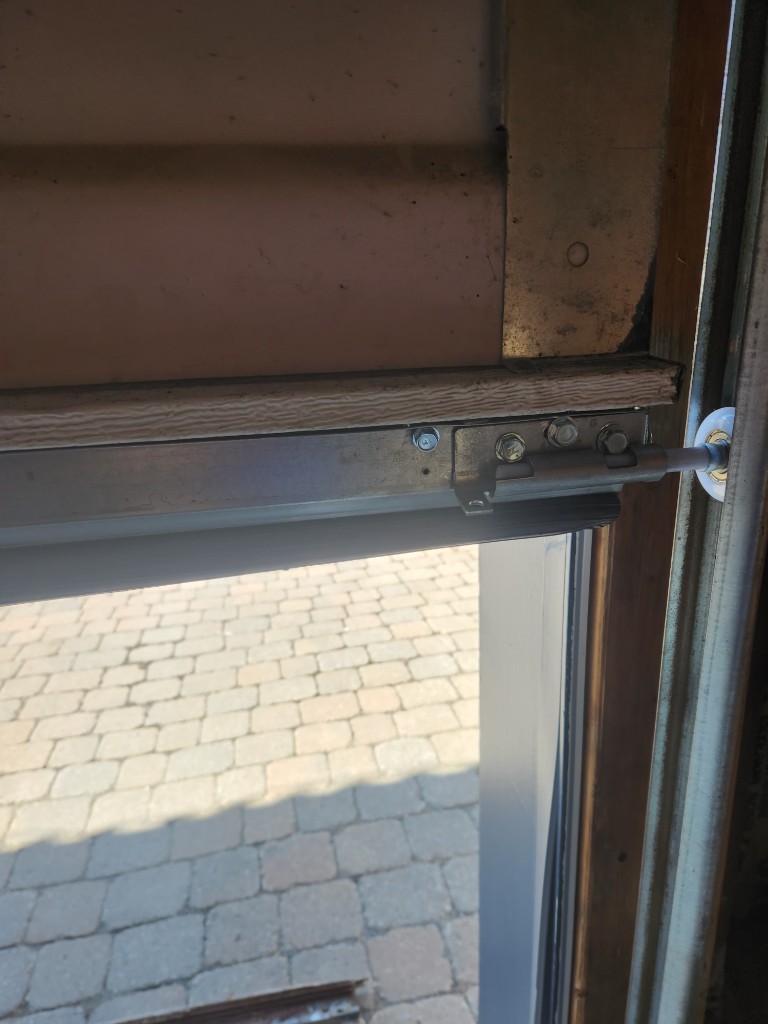 Close-up of garage door bottom weather seal with aluminum retainer and black rubber U-seal, professional installation