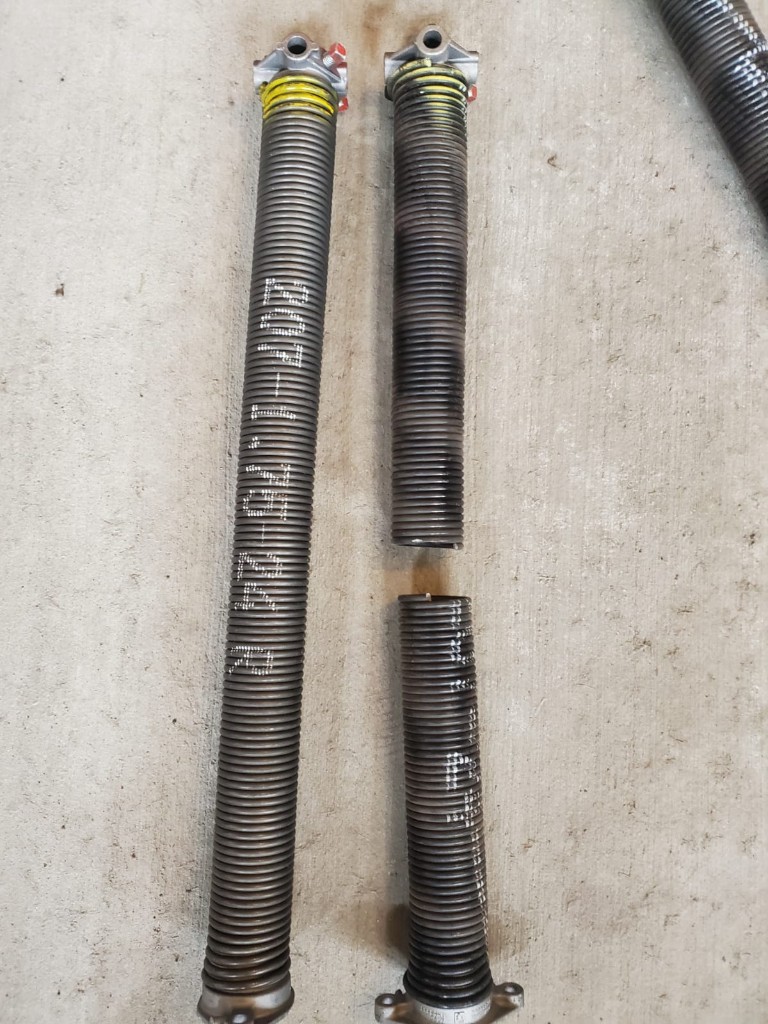 Broken torsion garage door spring next to a new replacement spring on a concrete floor in Ottawa