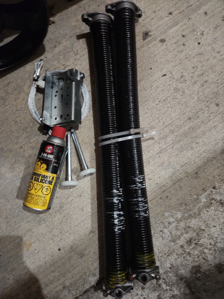 Garage door repair parts laid out for a complete service — springs, cables, rollers, and lubricant by GDS Ottawa