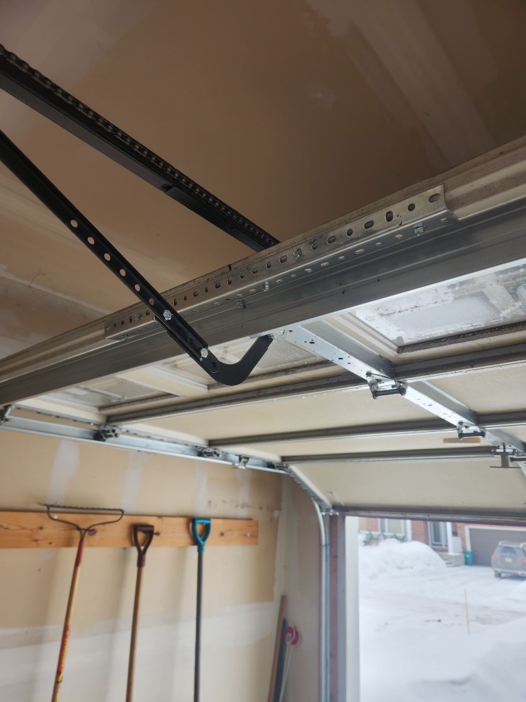 Garage door panel reinforcement strut installed on top section in Kanata — opener arm bracket secured to aluminum brace