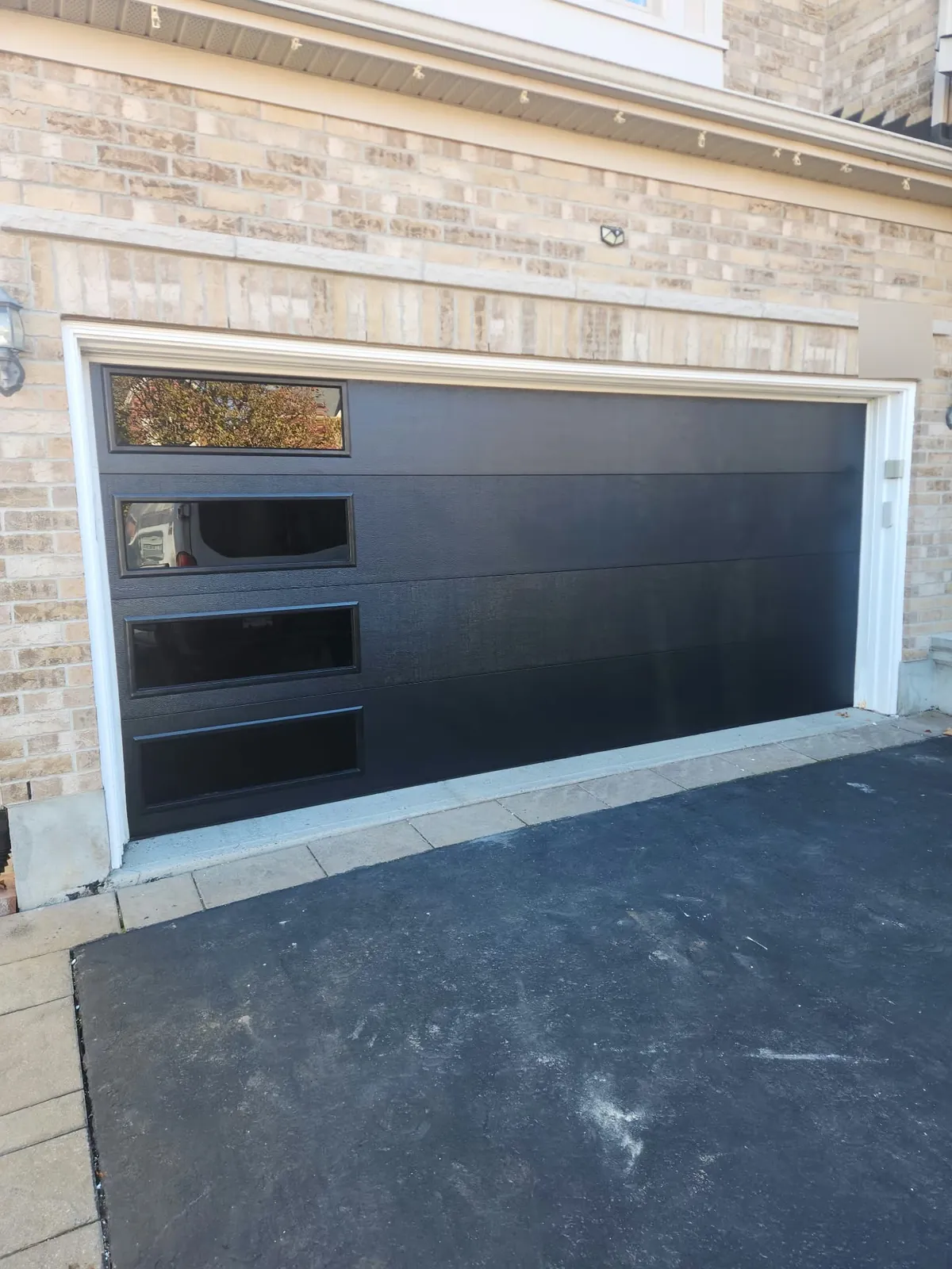 New black contemporary garage door with offset windows on a brick Nepean home