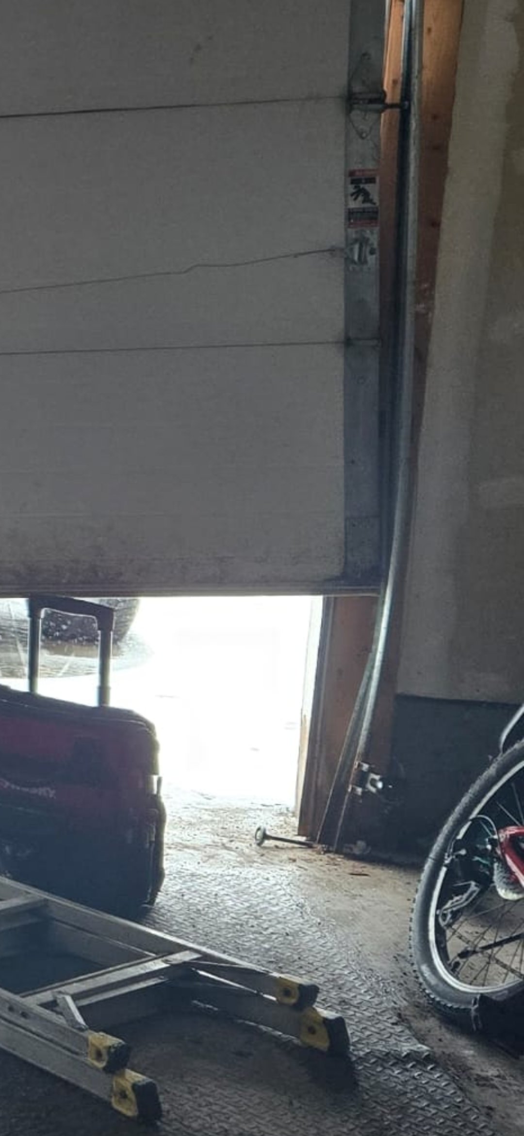 Bent garage door vertical track with roller out of the rail; white door crooked in Ottawa garage — before track repair