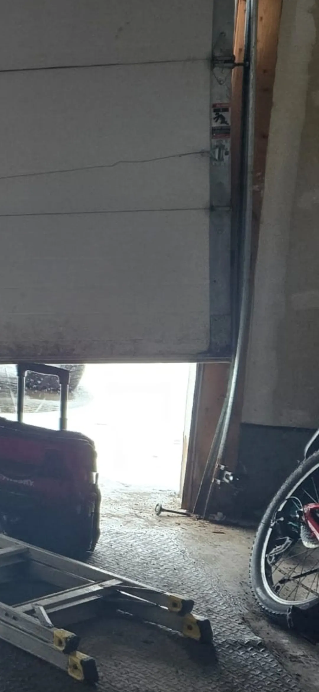 Bent garage door vertical track with roller out of the rail; white door crooked in Ottawa garage — before track repair
