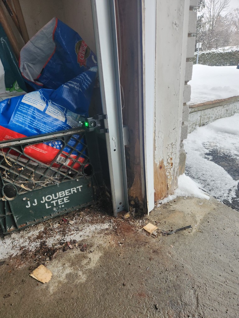 Rotted wooden garage door jamb and vertical track base with moisture damage in Ottawa