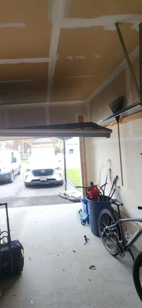 Off-track garage door emergency repair in Ottawa — black door hanging at a steep angle inside the garage